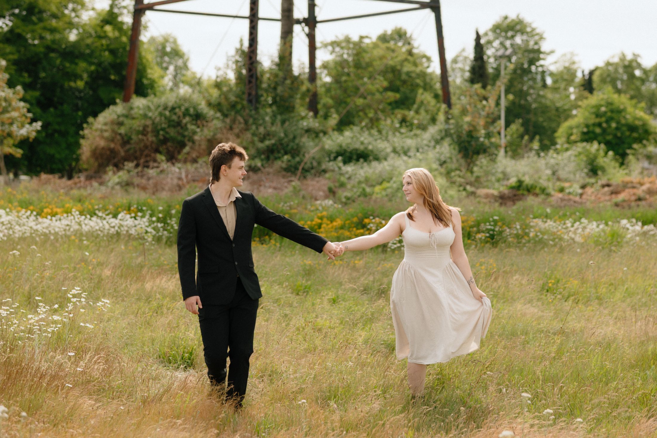 Claire and Evan walking hand in hand through a meadow
